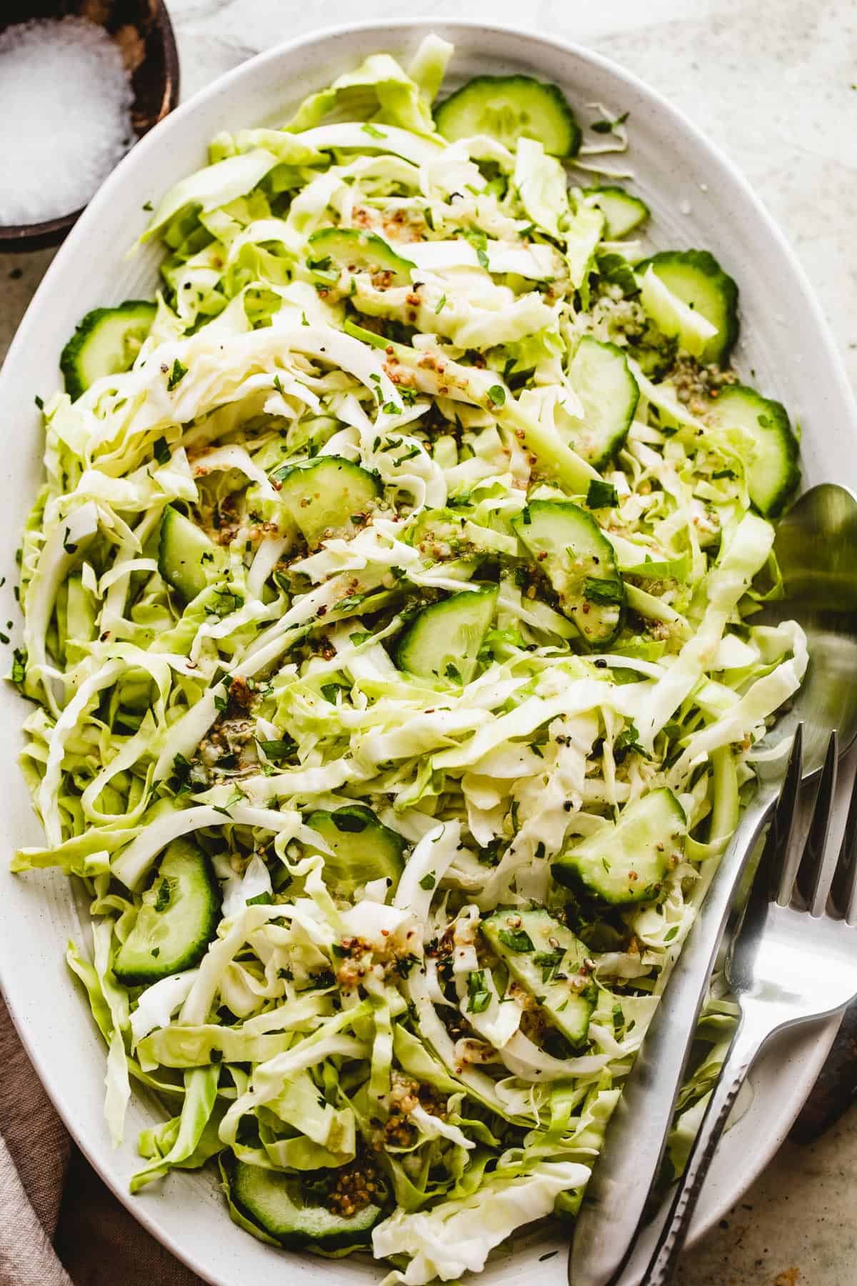 Cabbage Cucumber Salad served on an oblong serving plate with a large fork and spoon placed to the side of the salad.