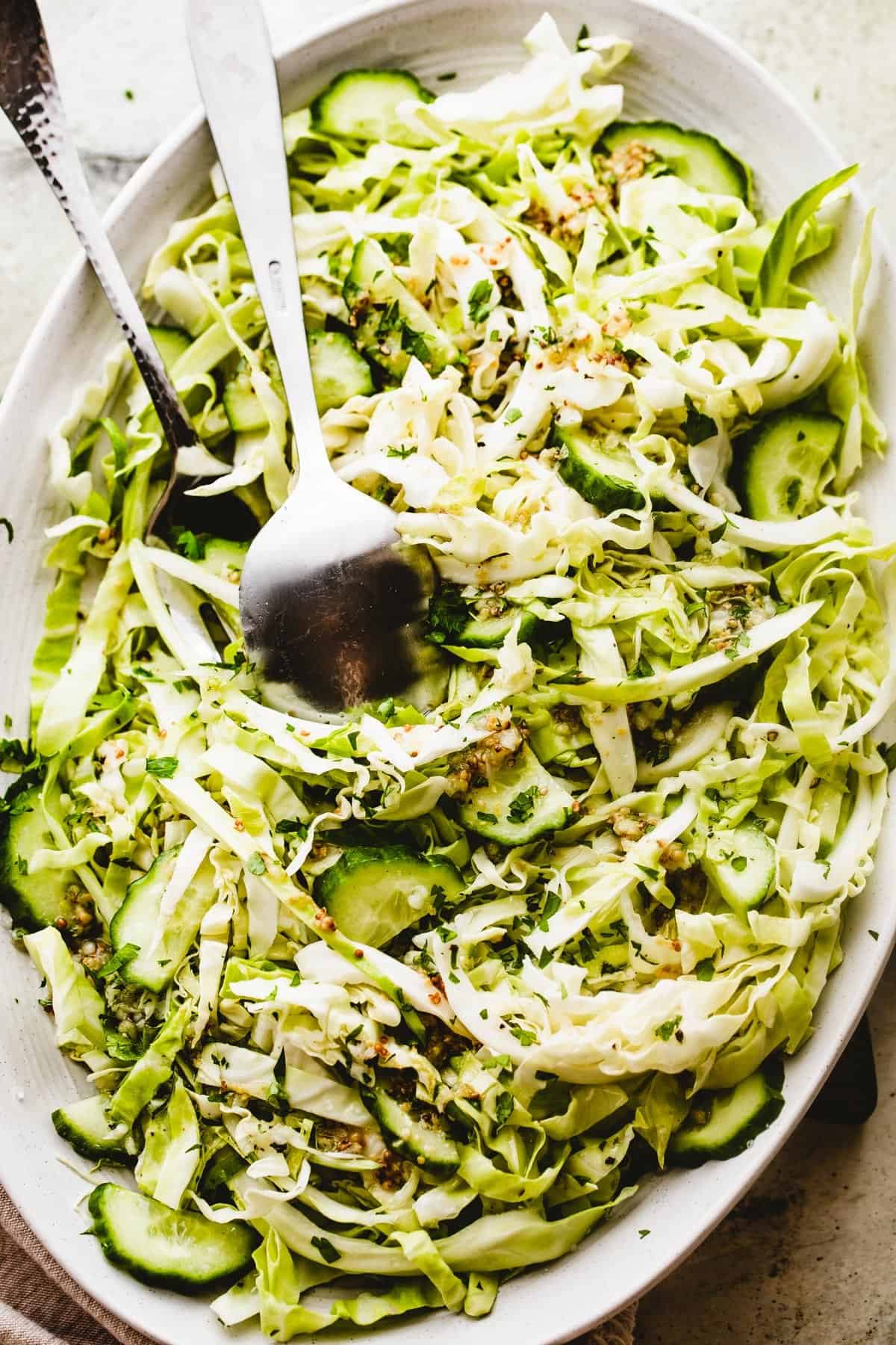 Cabbage Cucumber Salad served on an oblong serving plate with a large fork and spoon placed in the center of the salad.