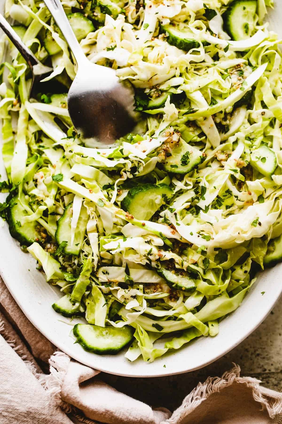 Cabbage Cucumber Salad served on an oblong serving plate with a large fork and spoon placed in the center of the salad.