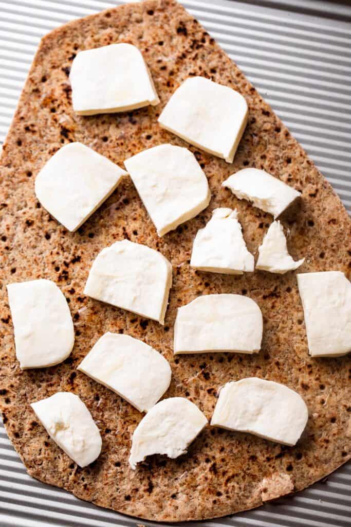 overhead shot of oval shaped flatbread topped with cubes of fresh mozzarella.