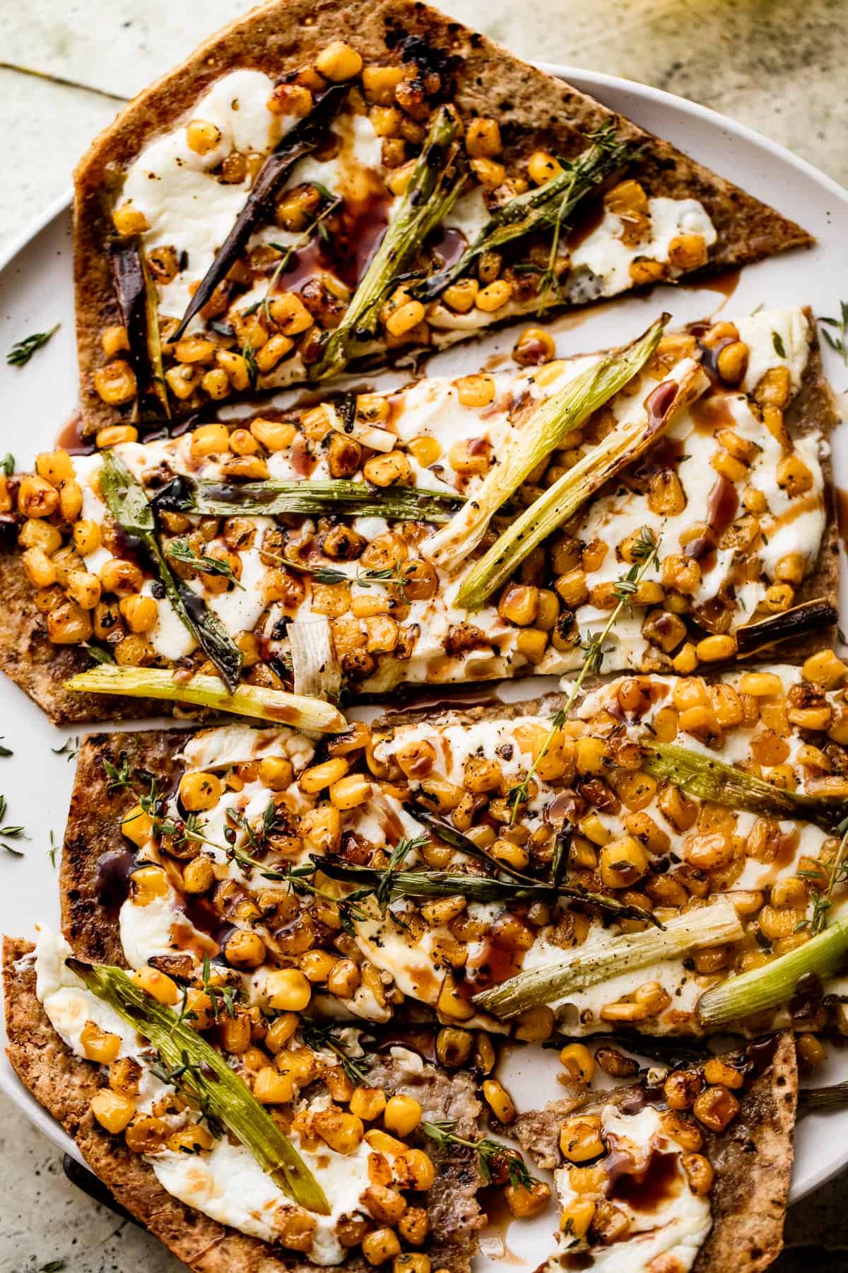 up close shot of grilled flatbread pizza topped with melted mozzarella, grilled corn kernels, and halved green onions scattered on top, and balsamic