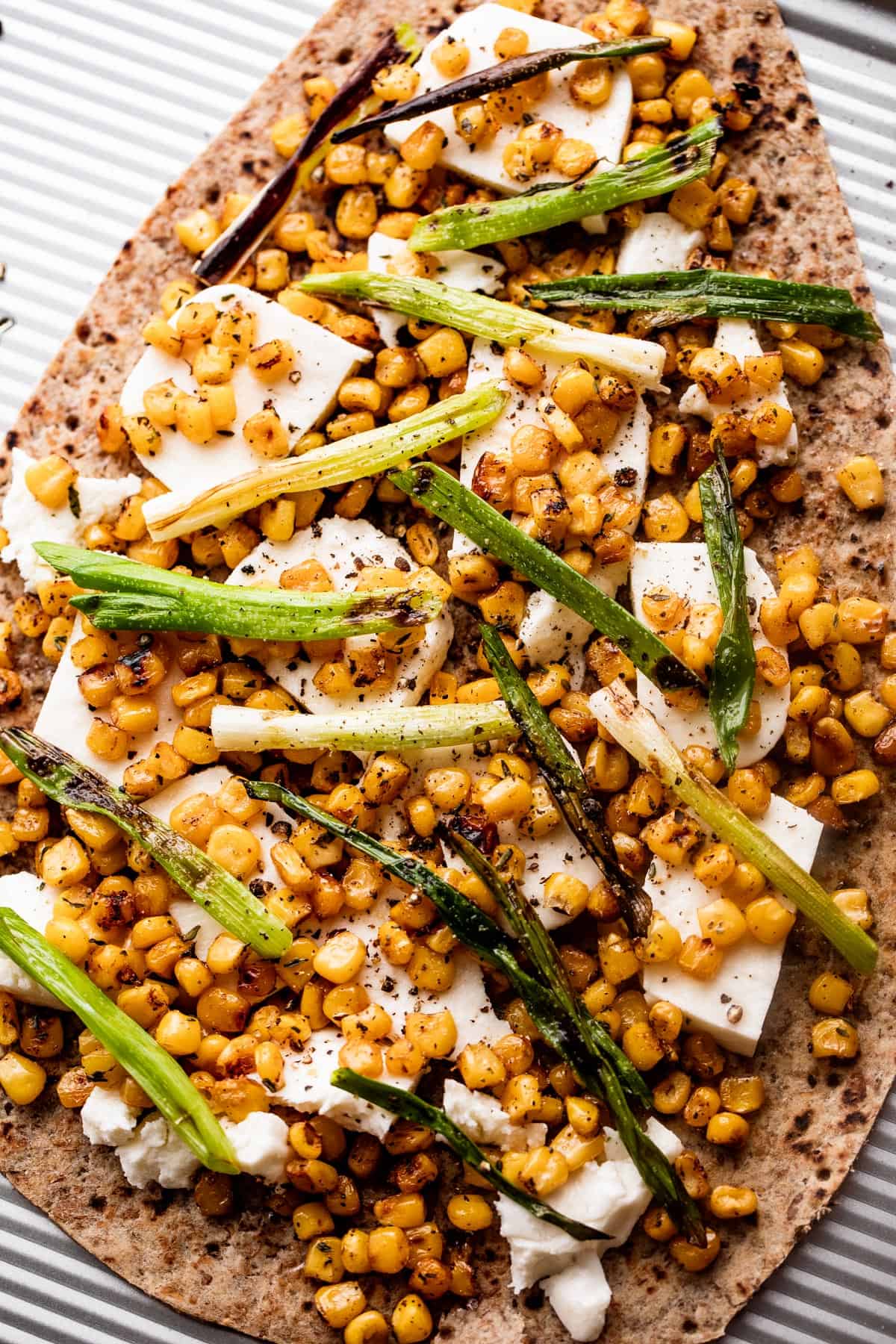 overhead shot of oval shaped flatbread topped with fresh mozzarella chunks, grilled corn kernels, and halved green onions scattered on top.