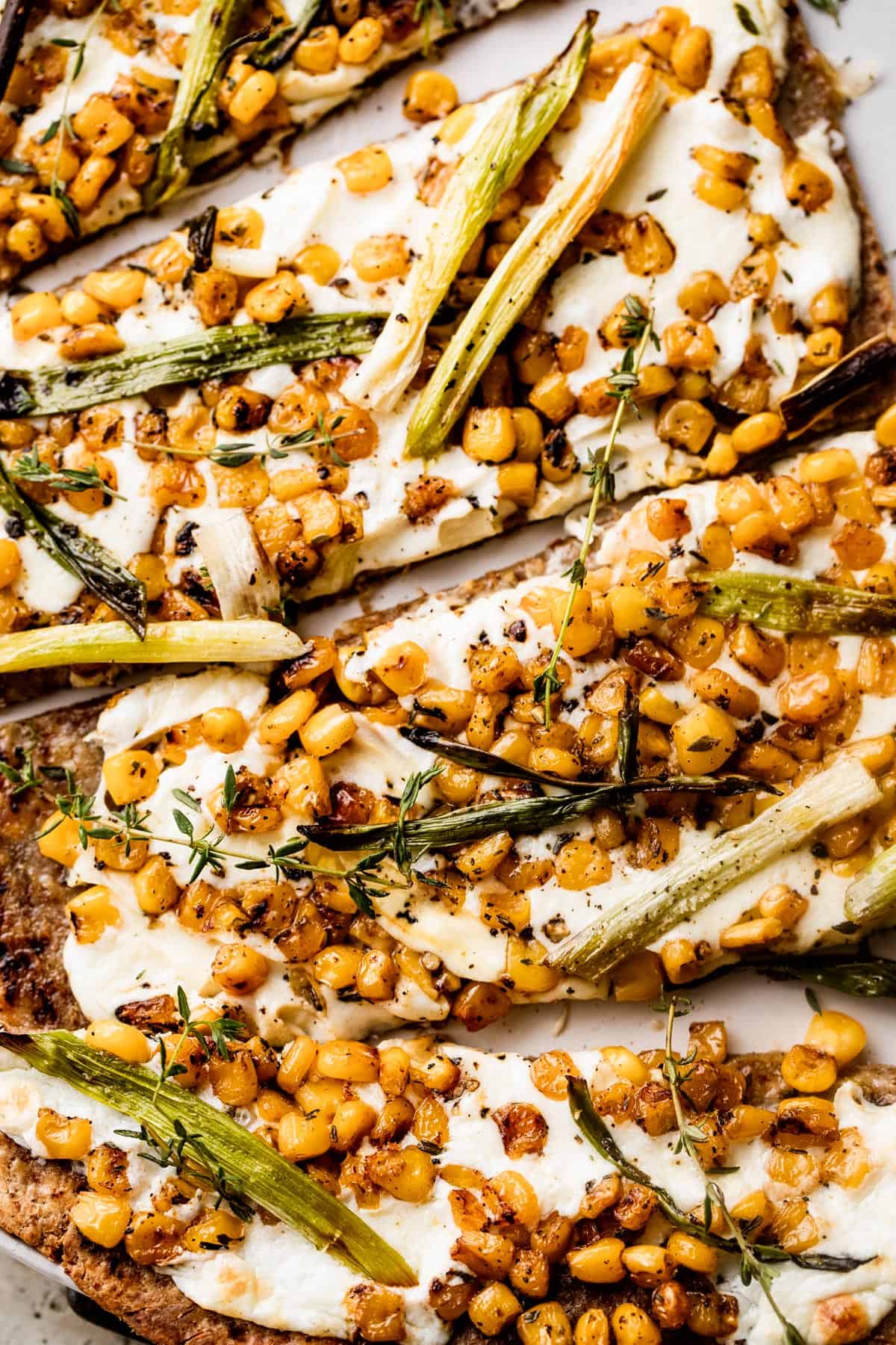 up close shot of grilled flatbread pizza topped with melted mozzarella, grilled corn kernels, and halved green onions scattered on top.