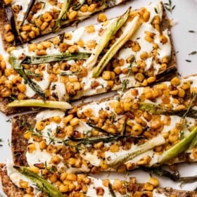 overhead shot of grilled flatbread pizza topped with melted mozzarella, grilled corn kernels, and halved green onions scattered on top, and balsamic