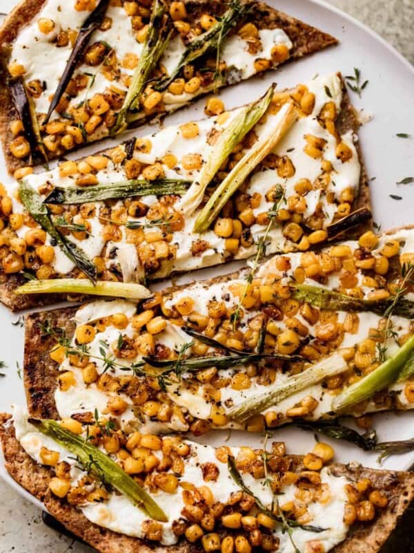 overhead shot of grilled flatbread pizza topped with melted mozzarella, grilled corn kernels, and halved green onions scattered on top, and balsamic