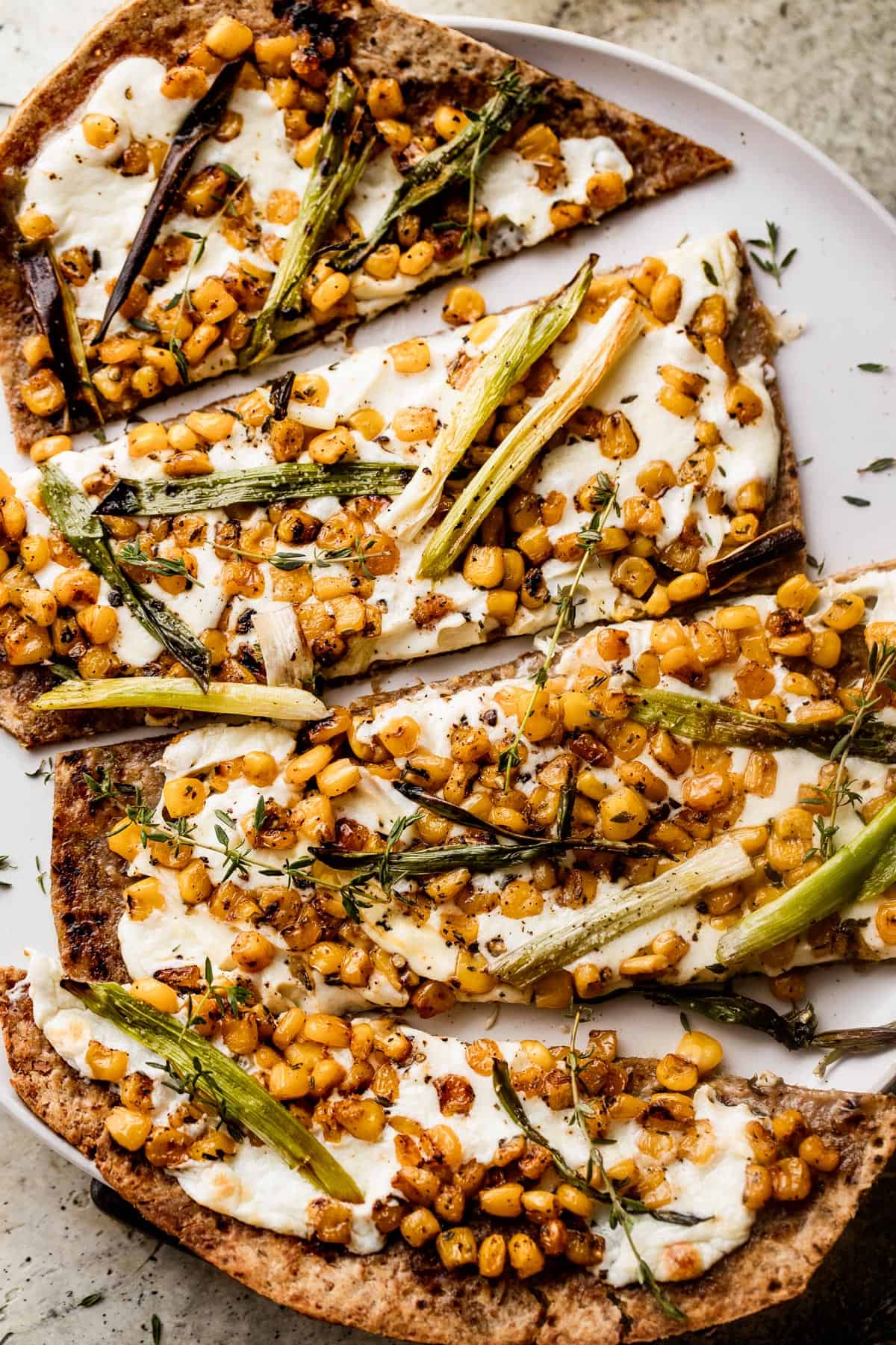 overhead shot of grilled flatbread pizza topped with melted mozzarella, grilled corn kernels, and halved green onions scattered on top, and balsamic