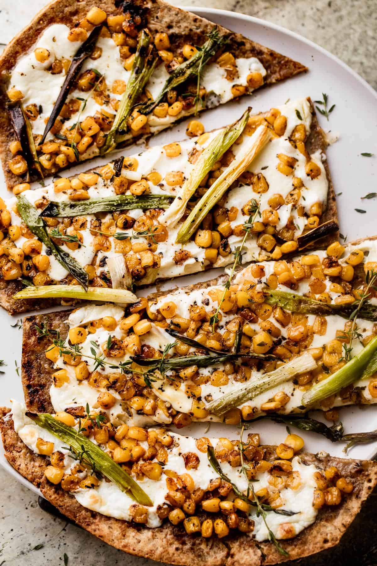 overhead shot of grilled flatbread pizza topped with  melted mozzarella, grilled corn kernels, and halved green onions scattered on top, and balsamic 