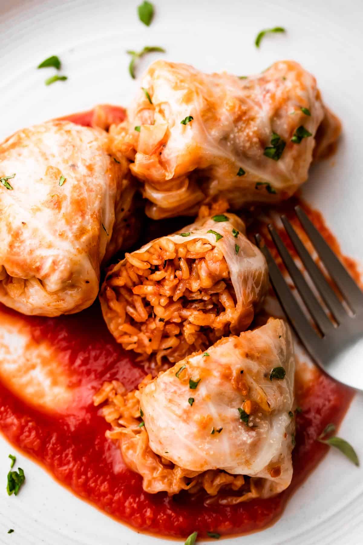a white plate with three cabbage rolls, and one of the cabbage rolls is cut in half.