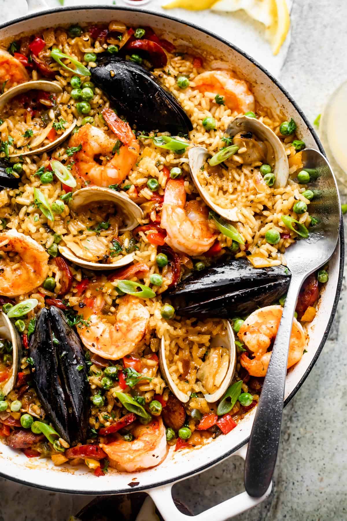 overhead shot of a braiser with spanish paella consisting of a bed of rice topped with clams, mussels, shrimp, peas, and sausages.
