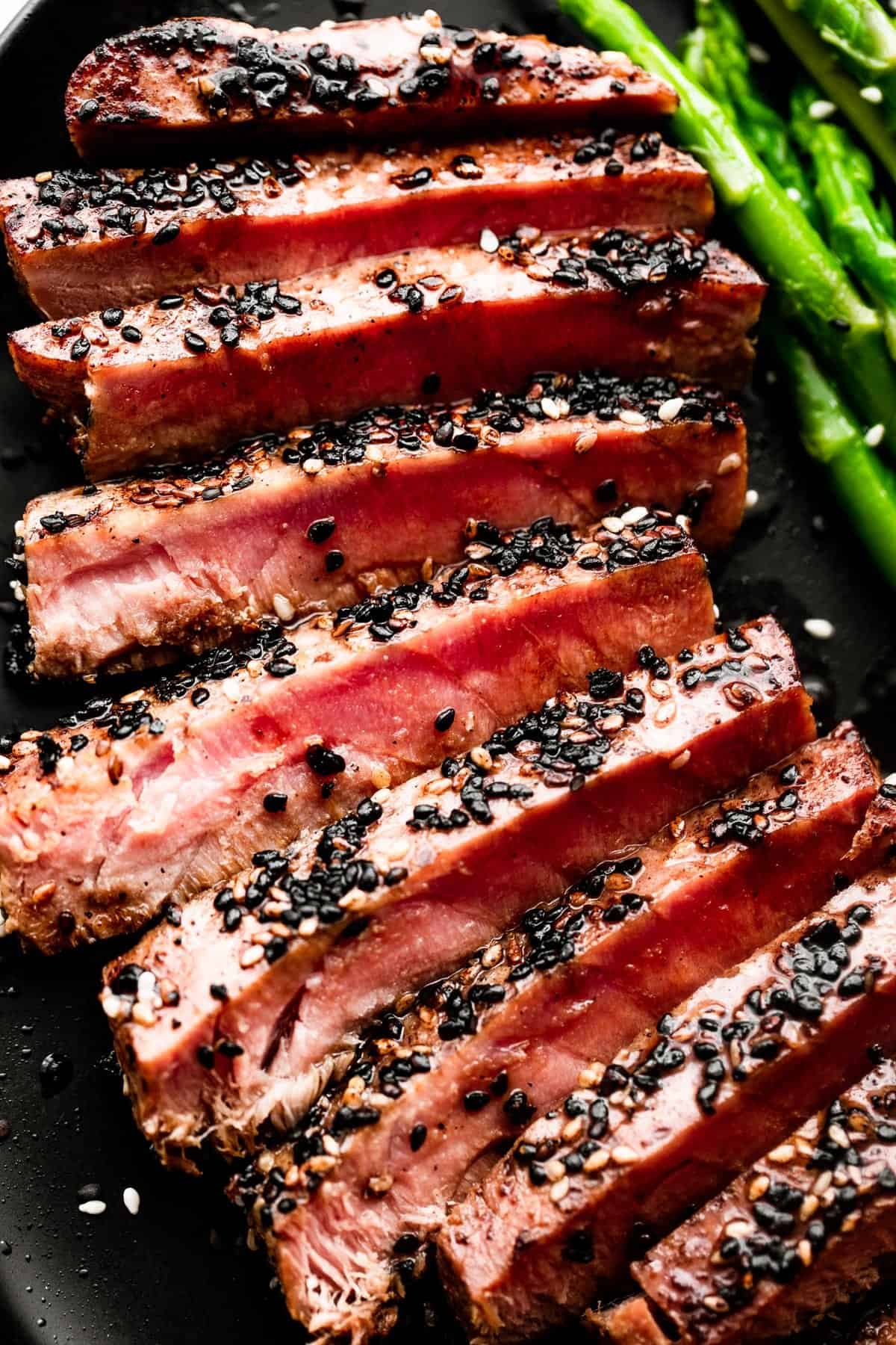 close up shot of sliced sesame crusted tuna steak served on a black dinner plate.