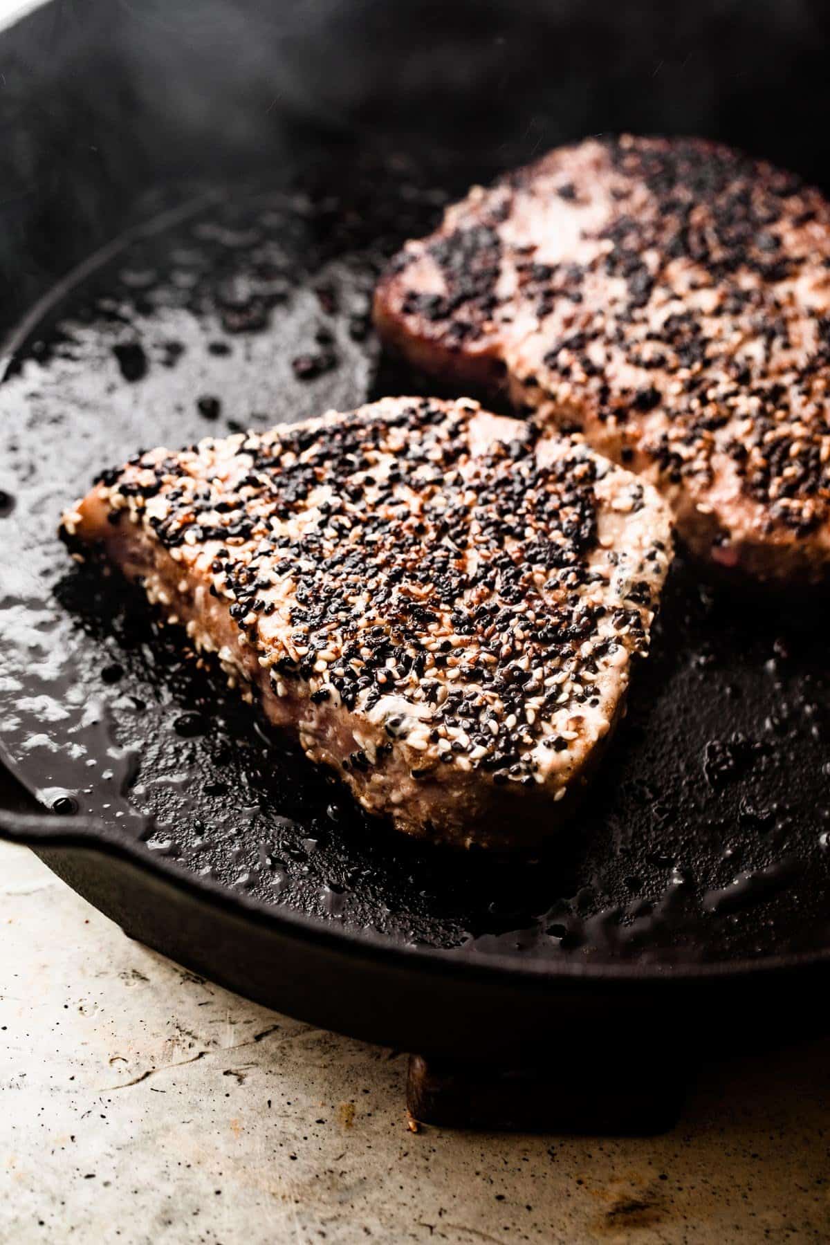 cooking two Sesame Crusted Tuna Steaks in a black cast iron skillet.
