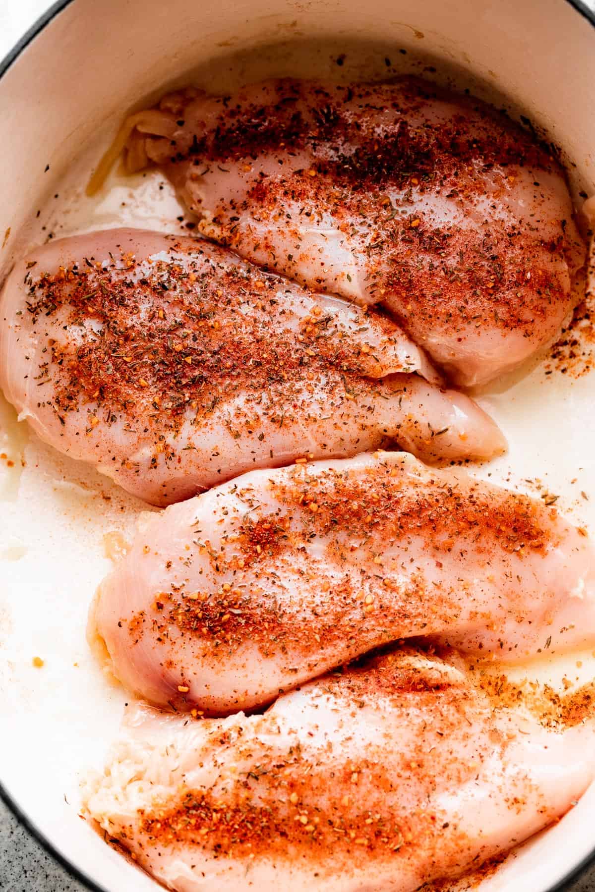 four raw chicken breasts arranged inside a white slow cooker insert.