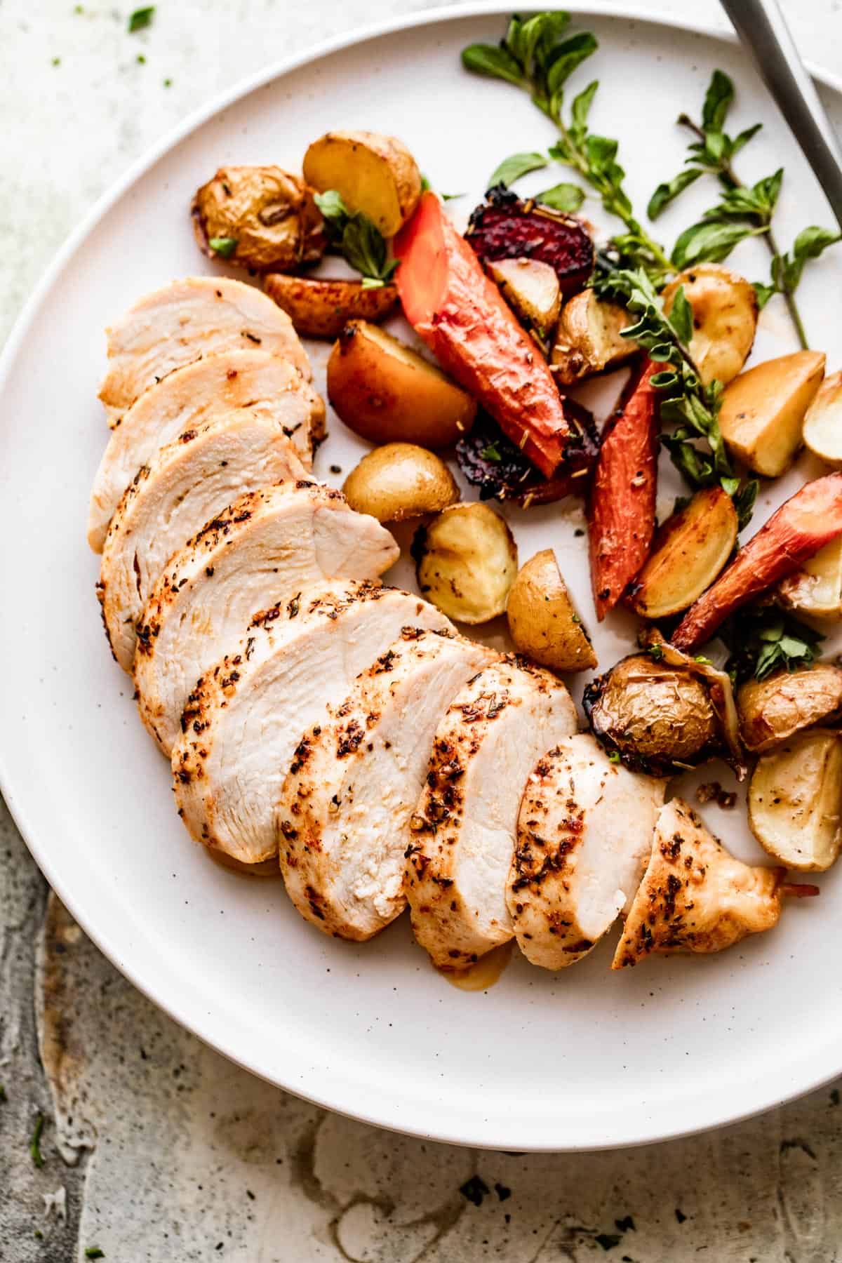 Dinner plate with sliced chicken breast on the left side of the plate, and roasted carrots and potatoes on the right side.