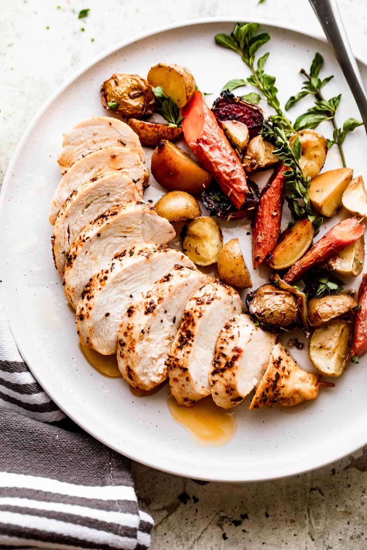 overhead shot of a dinner plate with sliced chicken breast on the left side of the plate, and roasted carrots and potatoes on the right side.