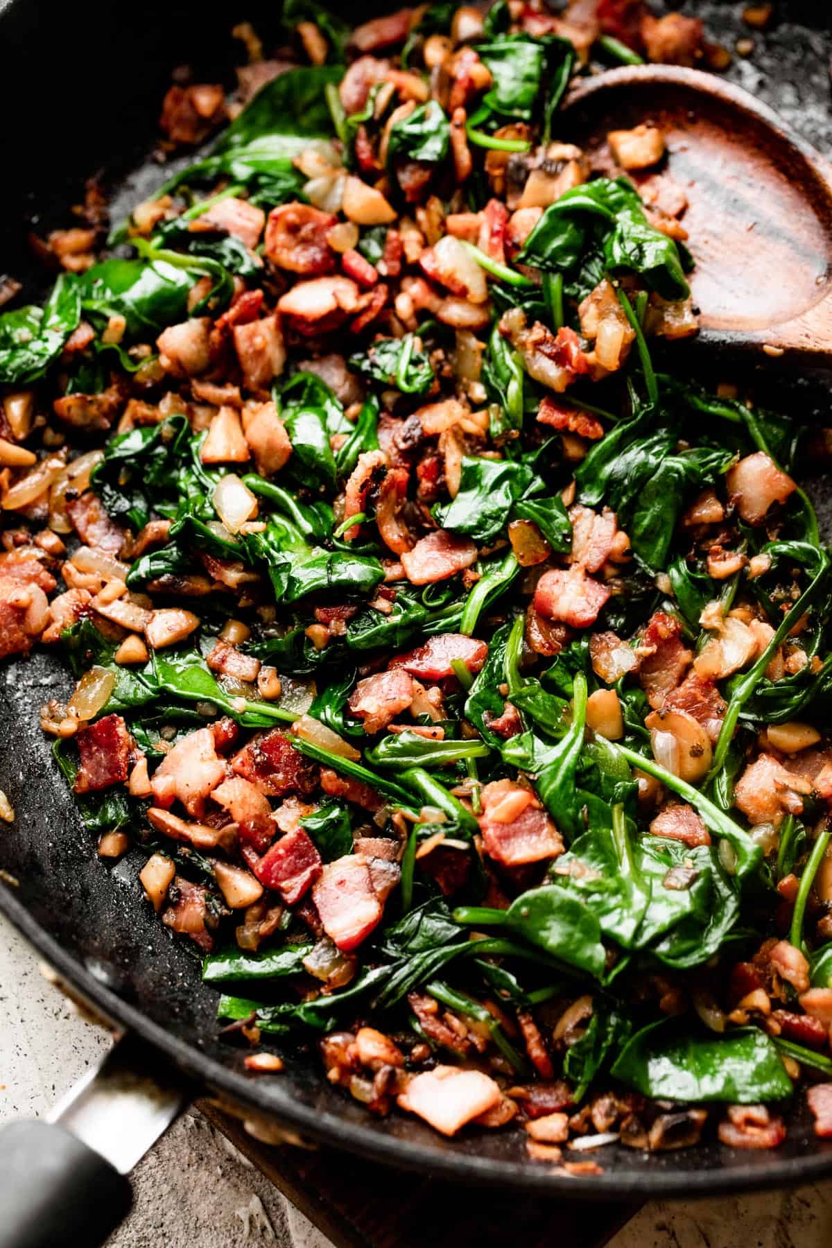 cooking diced bacon, chopped mushrooms, and baby spinach in a black skillet.