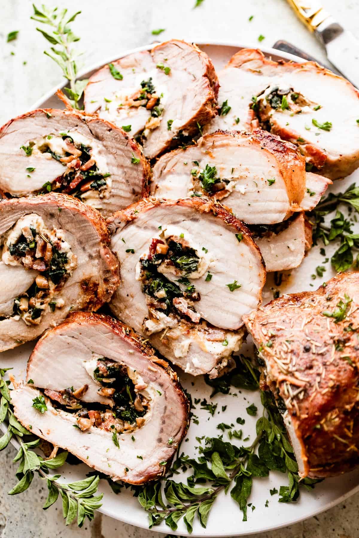 overhead shot of sliced stuffed pork loin arranged on a round white serving plate garnished with greens.