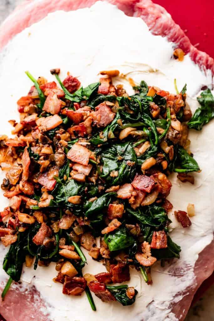 cooked mixture of diced bacon, baby spinach, and mushrooms arranged on top of a butterflied pork