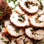 overhead shot of sliced stuffed pork loin arranged on a round white serving plate garnished with greens.