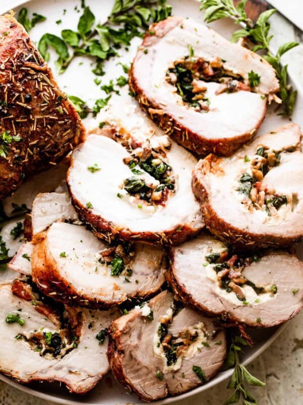 overhead shot of sliced stuffed pork loin arranged on a round white serving plate garnished with greens.