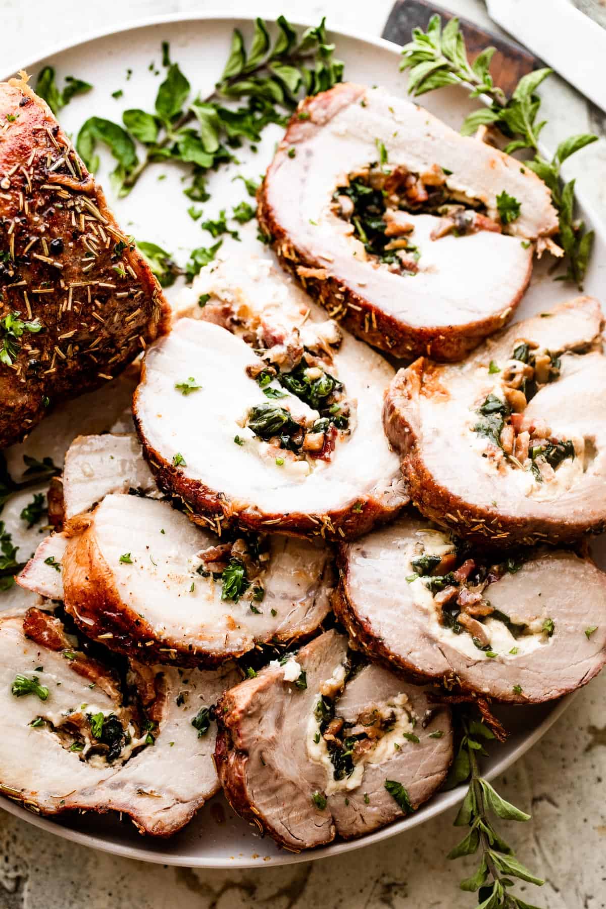 overhead shot of sliced stuffed pork loin arranged on a round white serving plate garnished with greens.