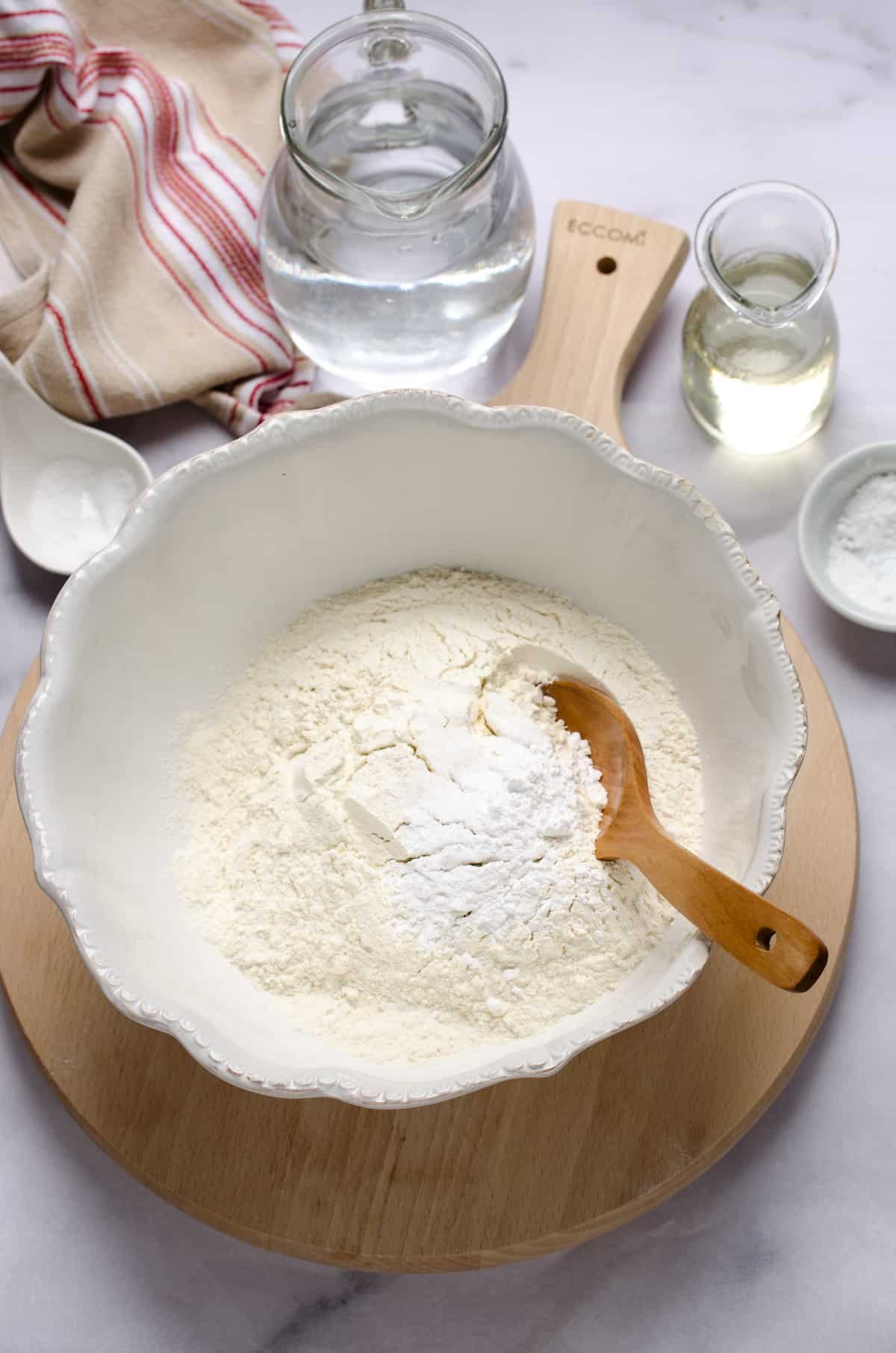 A wooden spoon combining the dry pizza dough ingredients in a mixing bowl