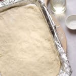 A foil-lined baking dish with no-yeast pizza dough spread into the bottom