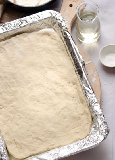 A foil-lined baking dish with no-yeast pizza dough spread into the bottom