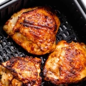 overhead shot of three cooked chicken thighs placed inside a black air fryer basket.
