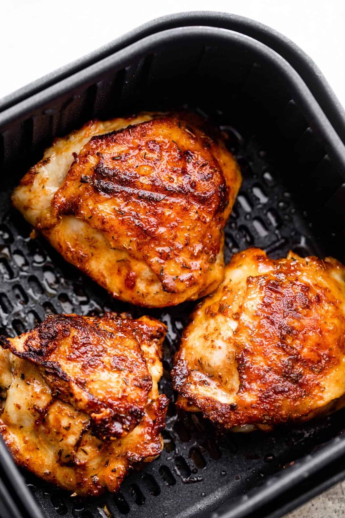 overhead shot of three cooked chicken thighs placed inside a black air fryer basket.