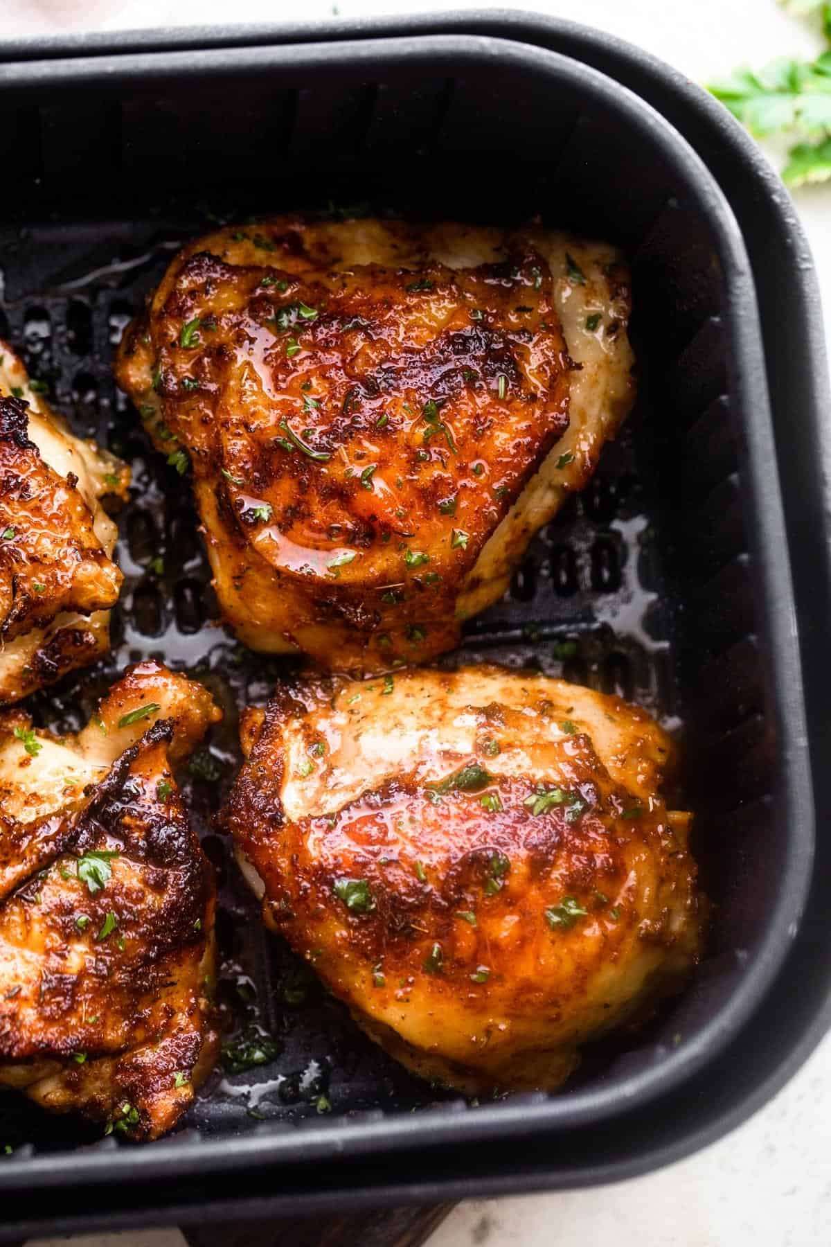 overhead shot of four cooked chicken thighs placed inside a black air fryer basket.