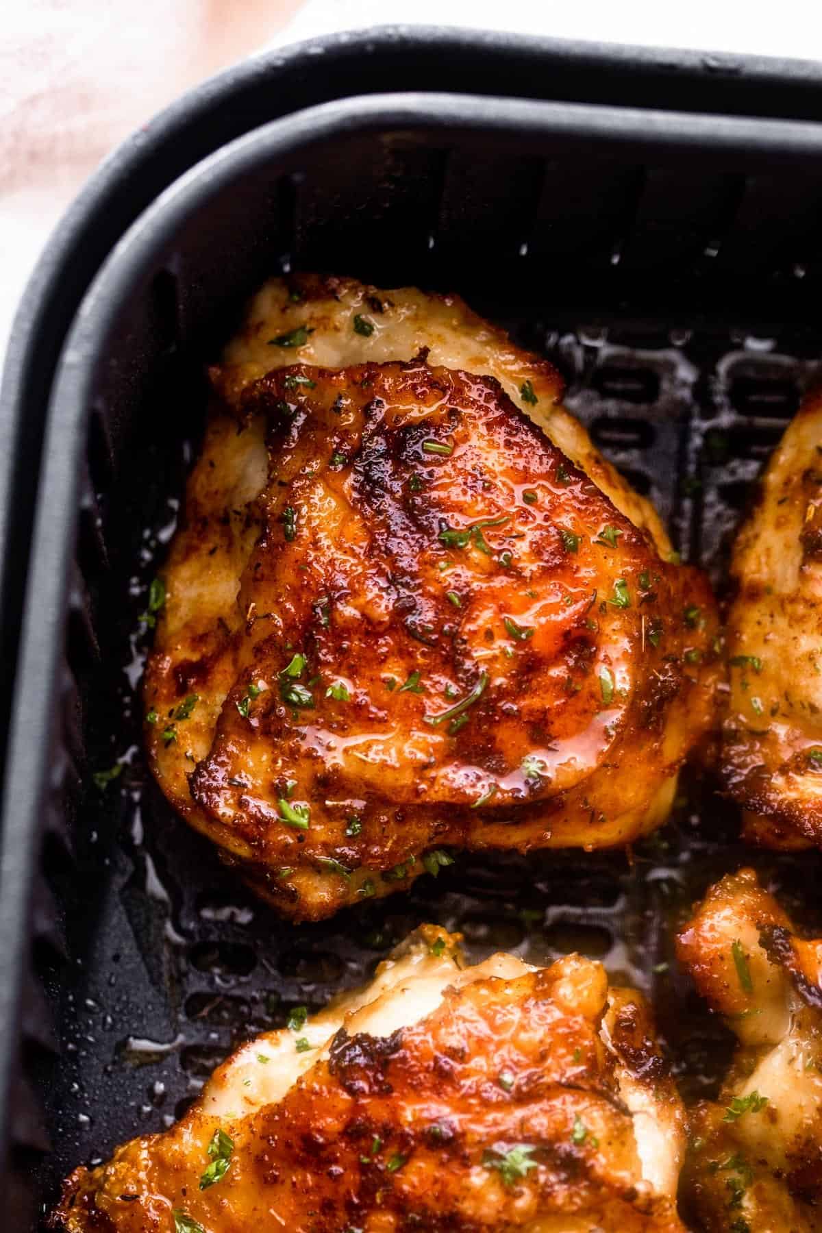 overhead close up shot of cooked chicken thighs placed inside a black air fryer basket.