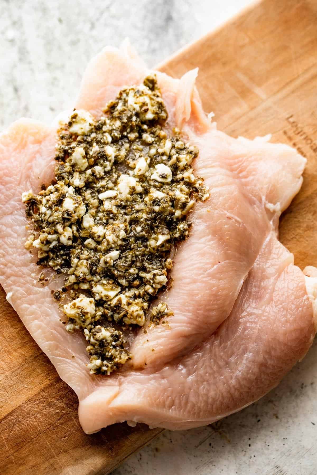 feta cheese and basil pesto mixture spread on a butterflied raw chicken breast