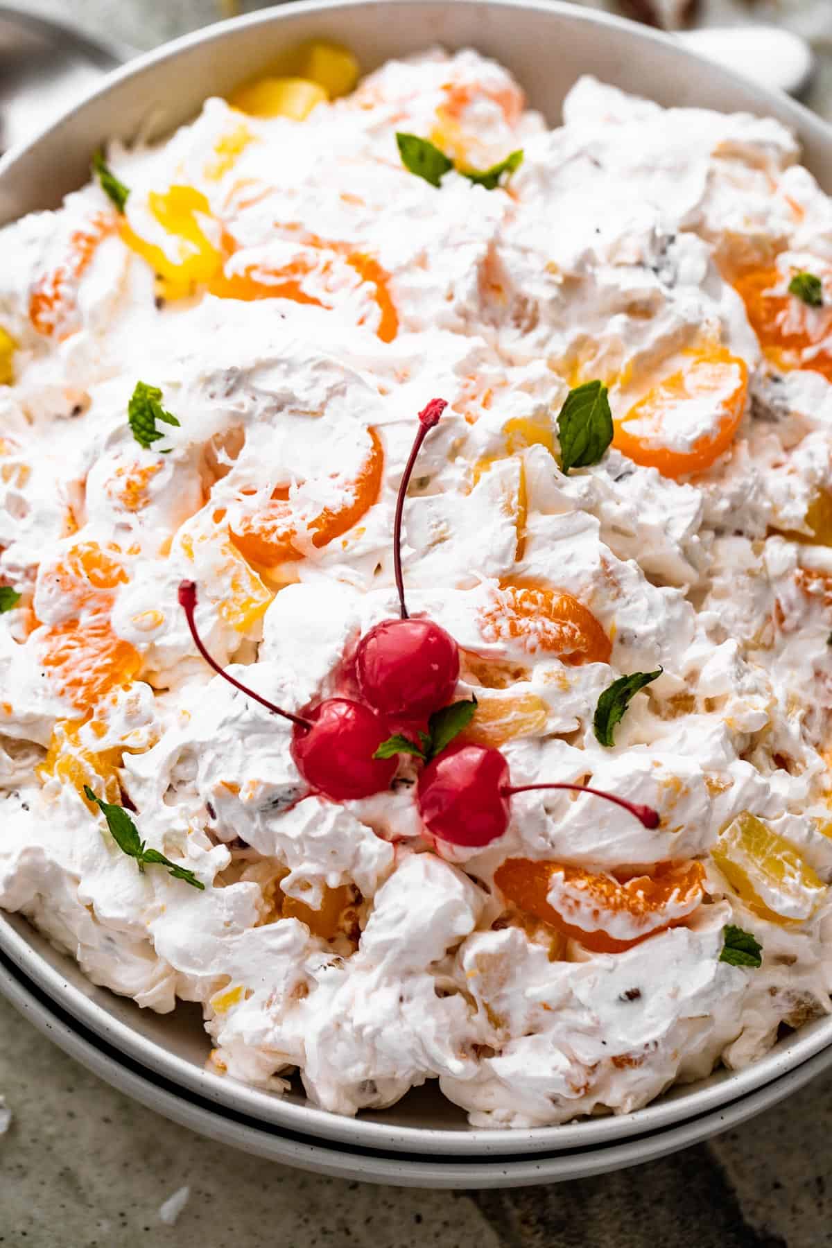 close up overhead shot of Ambrosia Salad served in a white dish and topped with three maraschino cherries and mint leaves.