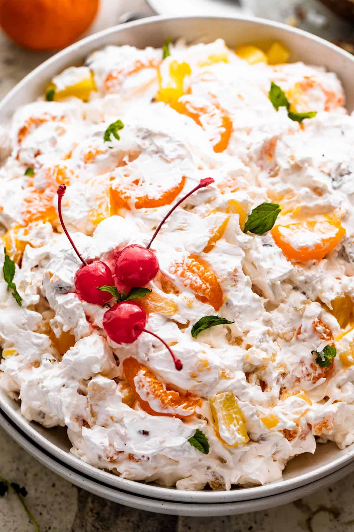 close up overhead shot of Ambrosia Salad served in a white dish and topped with three maraschino cherries and mint leaves.