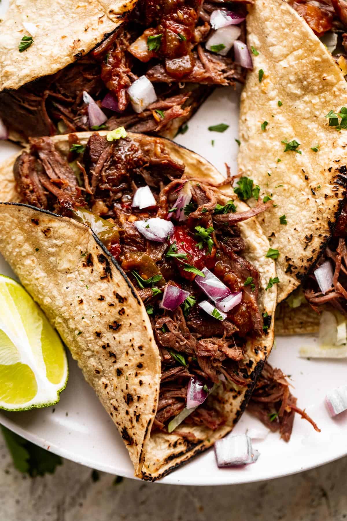 up close shot of Slow Cooker Beef Machaca taco served in corn tortillas and topped with diced red onions.