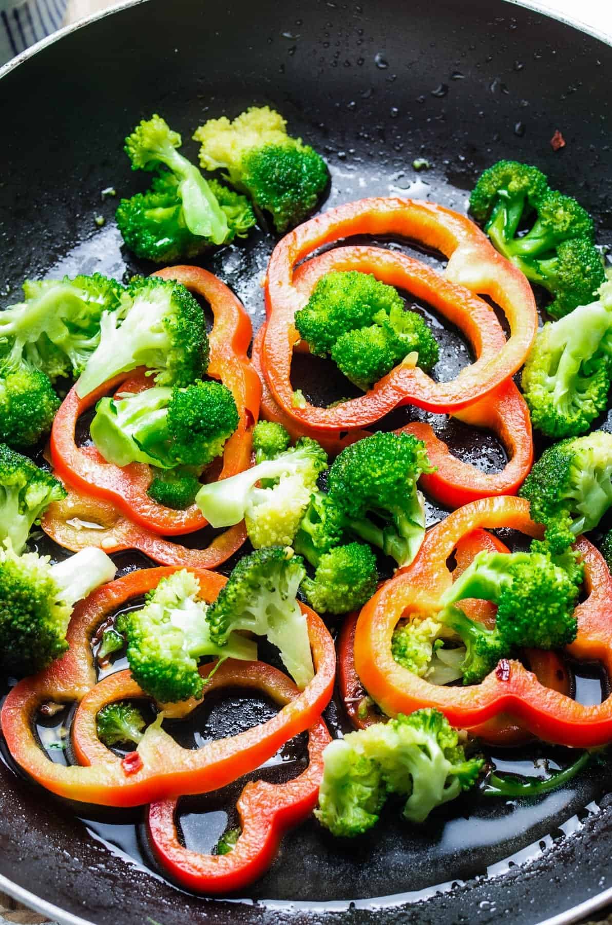 Broccoli florets and sliced peppers inside of a saucepan with vegetable oil.