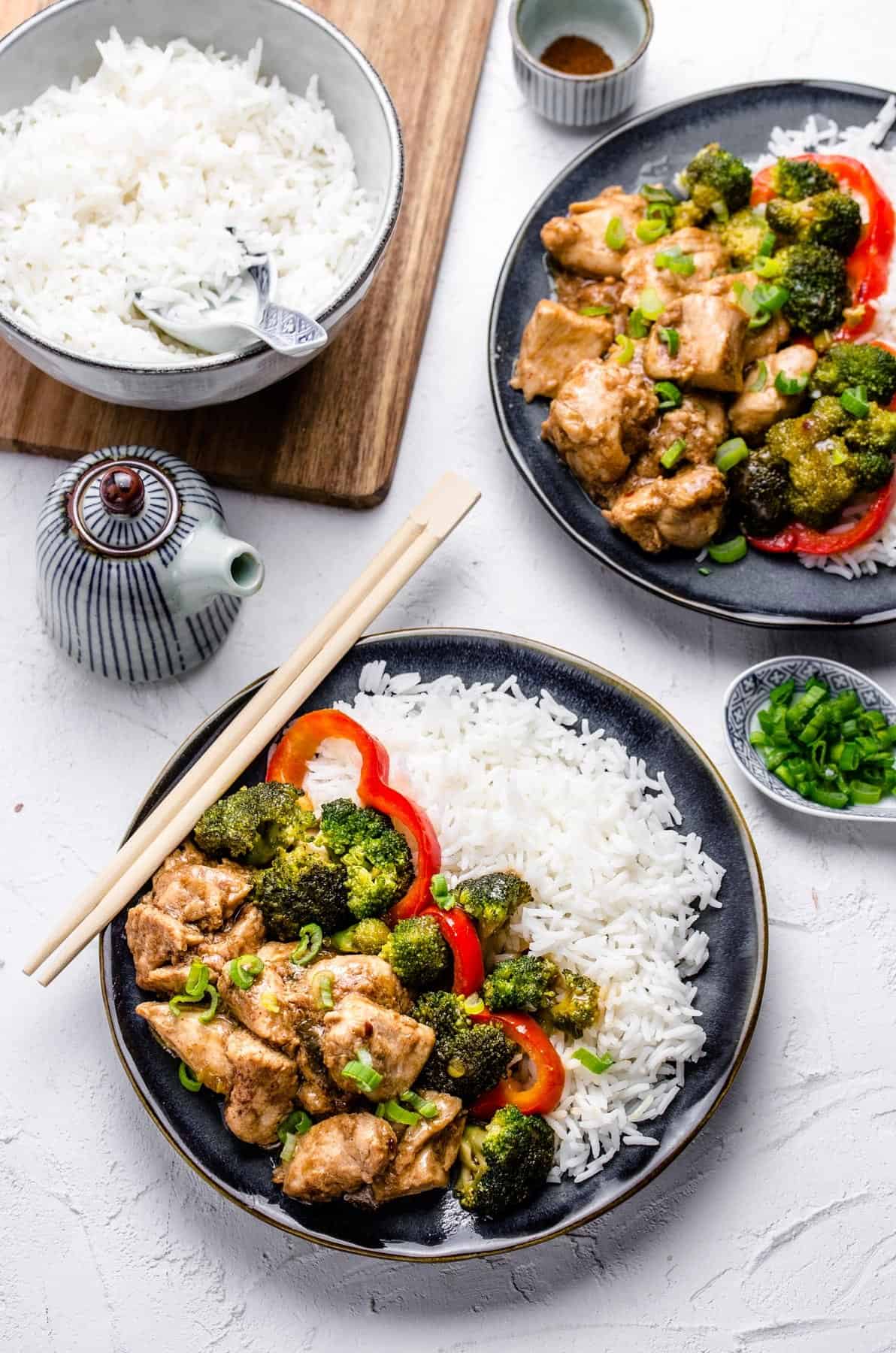 A plate of chicken, rice and vegetables beside a small teapot.