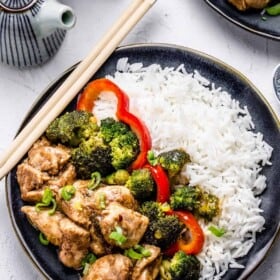 A plate of Chinese chicken and broccoli with white rice and a pair of chopsticks
