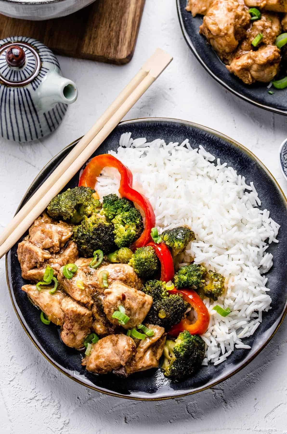 A plate of Chinese chicken and broccoli with white rice and a pair of chopsticks