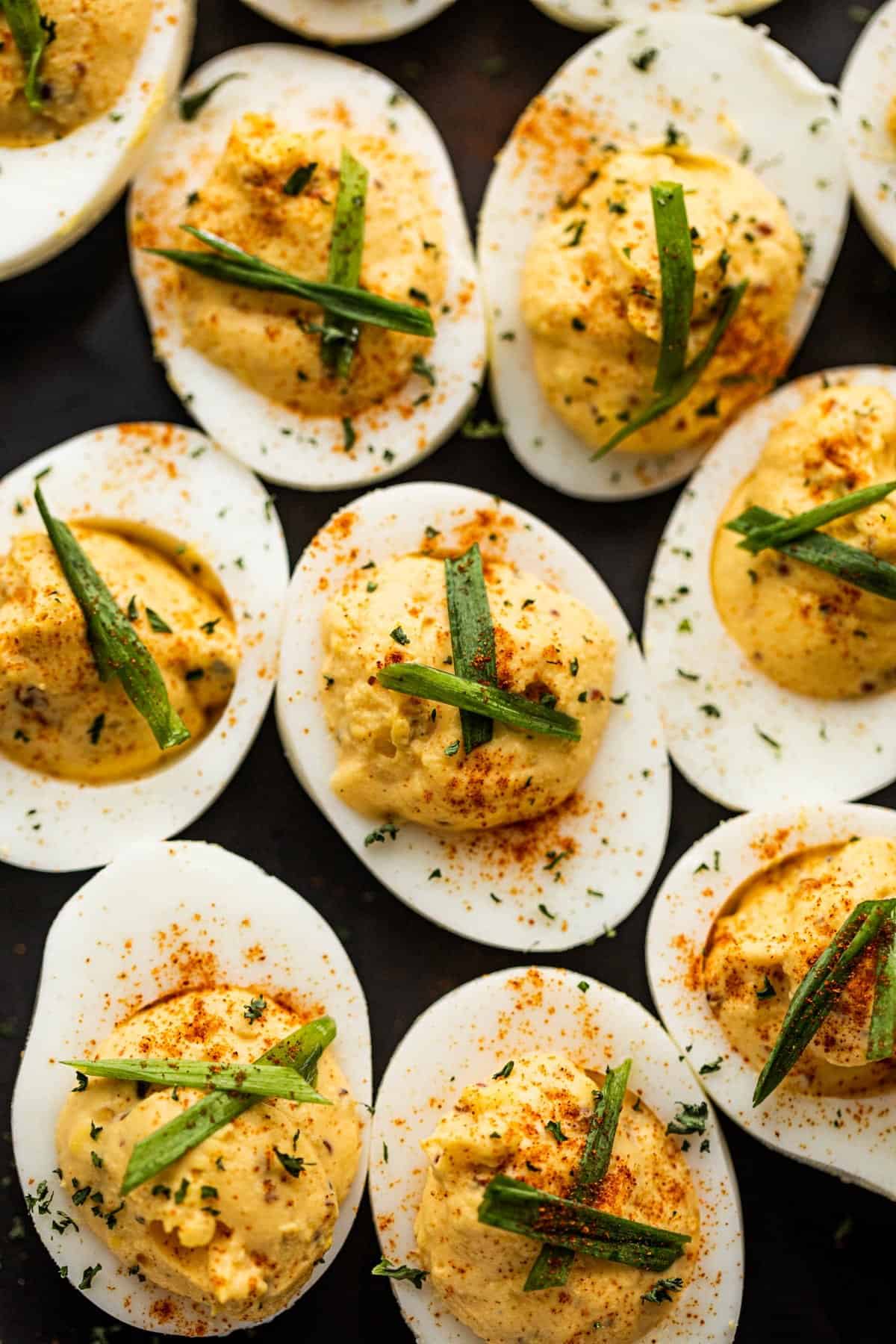 classic deviled eggs arranged on a black background and topped with paprika and chives.