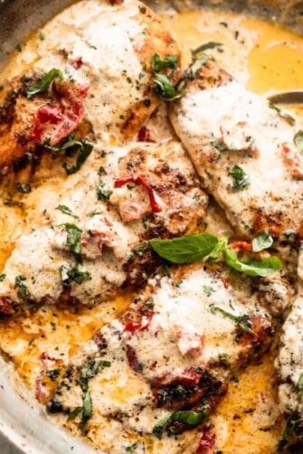 four chicken cutlets arranged in a skillet with creamy sauce and sundried tomatoes.