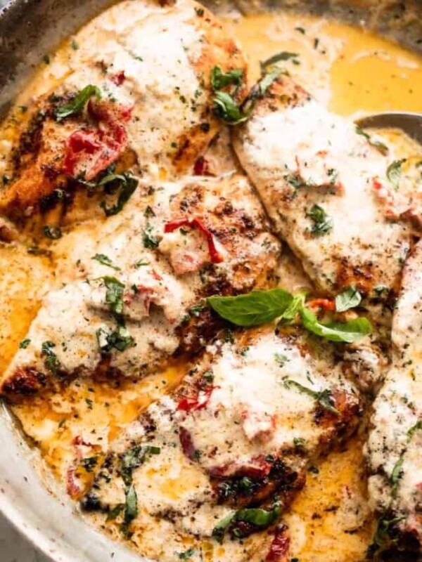 four chicken cutlets arranged in a skillet with creamy sauce and sundried tomatoes.