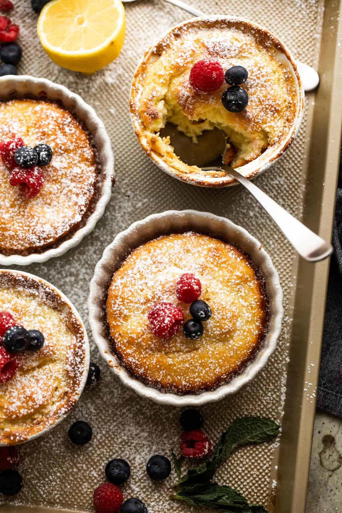 overhead shot of mini lemon cakes baked in ramekins, and topped with powdered sugar and berries.