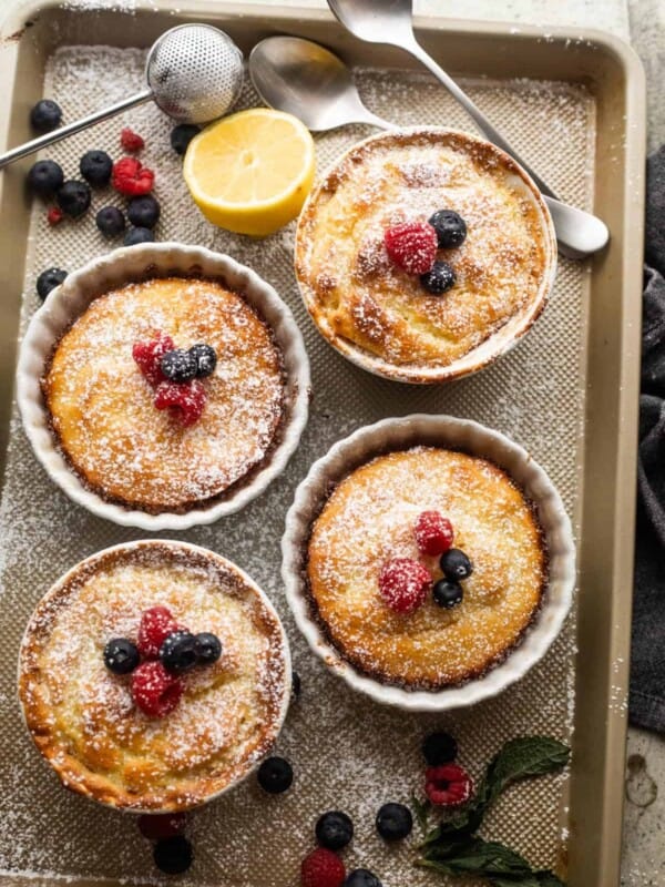 overhead shot of mini lemon cakes baked in ramekins, and topped with powdered sugar and berries.