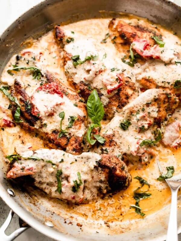 a skillet with five chicken cutlets in a creamy sauce with sundried tomatoes, and garnished with chopped basil.