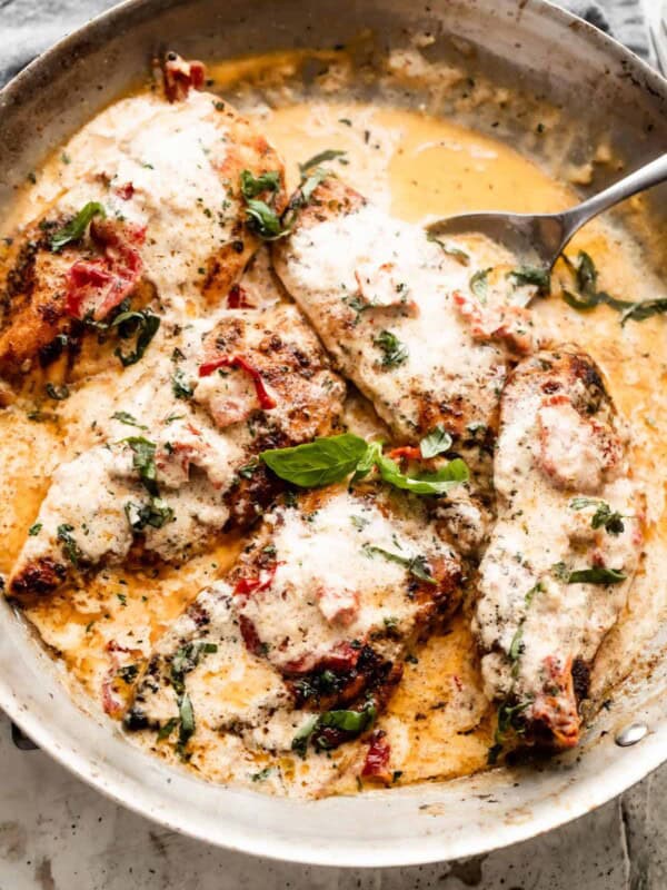 a skillet with five chicken cutlets in a creamy sauce with sundried tomatoes, and garnished with chopped basil.