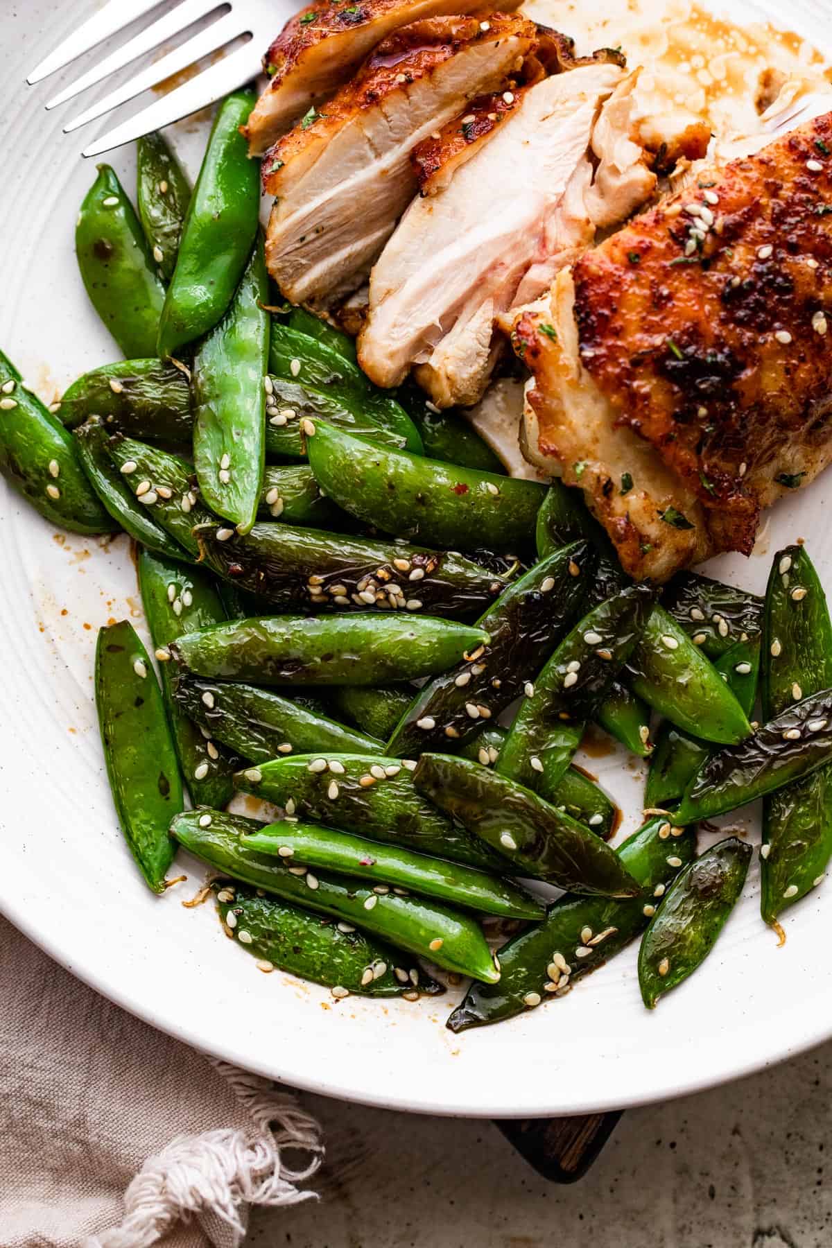 cooked sugar snap peas arranged on a dinner plate with chicken thighs placed next to them.