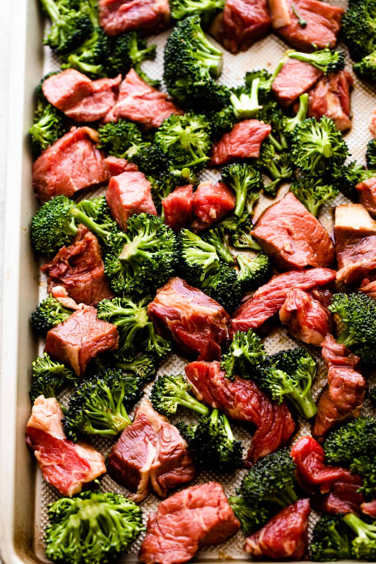 overhead shot of cubes of raw steak and broccoli on a sheet pan