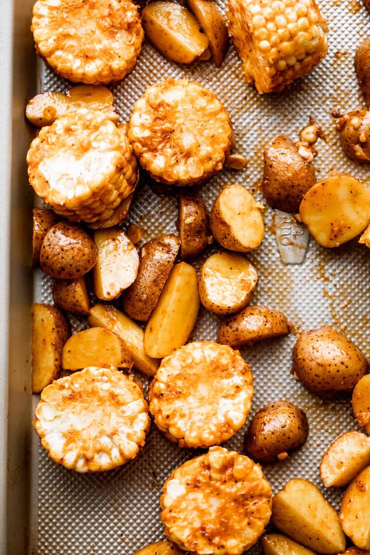 rounds of corn on the cob and quartered potatoes arranged on a sheet pan.