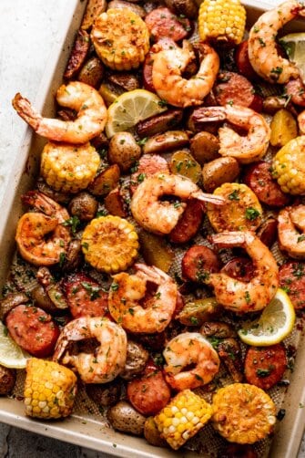 shrimp, potatoes, sausages, and corn arranged on a sheet pan and garnished with a few lemon slices.
